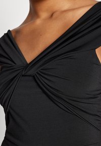 Schwarzes Stoffoberteil mit einem verdrehten Design am Kragen, mit Drapierung und weicher Textur, die das glatte Finish des Materials hervorhebt.