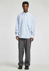 Jasnoniebieska koszula w paski na guziki z przednią kieszenią, zestawiona z szerokimi szarymi spodniami w prążki i czarnymi mokasynami.