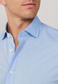 Lichtblauw overhem shirt met een subtiel stippenpatroon, gemaakt van soepel stof. Beschikt over een klassieke kraag en witte knopen.