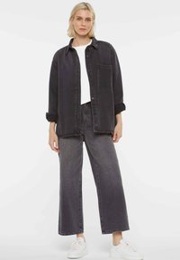 Black denim shirt paired with matching wide-leg black jeans. The shirt features a chest pocket and rolled sleeves. White sneakers complete the look.