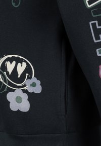 Zwarte trui met een voorzak met meerkleurige afbeeldingen: een glimlachend gezicht en bloemen in paarse en groene tinten.