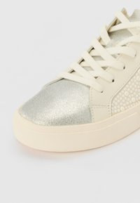 Ezüst textúrájú sneaker krém színű kiegészítőkkel, lekerekített orral és lapos fűzővel, díszített fehér gyöngyszerű tűzőgombokkal az oldalán.