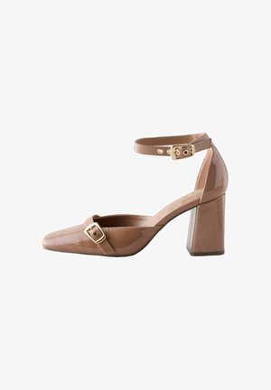 Scarpa con tacco alto in pelle verniciata marrone, punta affusolata, cinturino alla caviglia con fibbia dorata e tacco a blocco. Design classico con texture liscia.