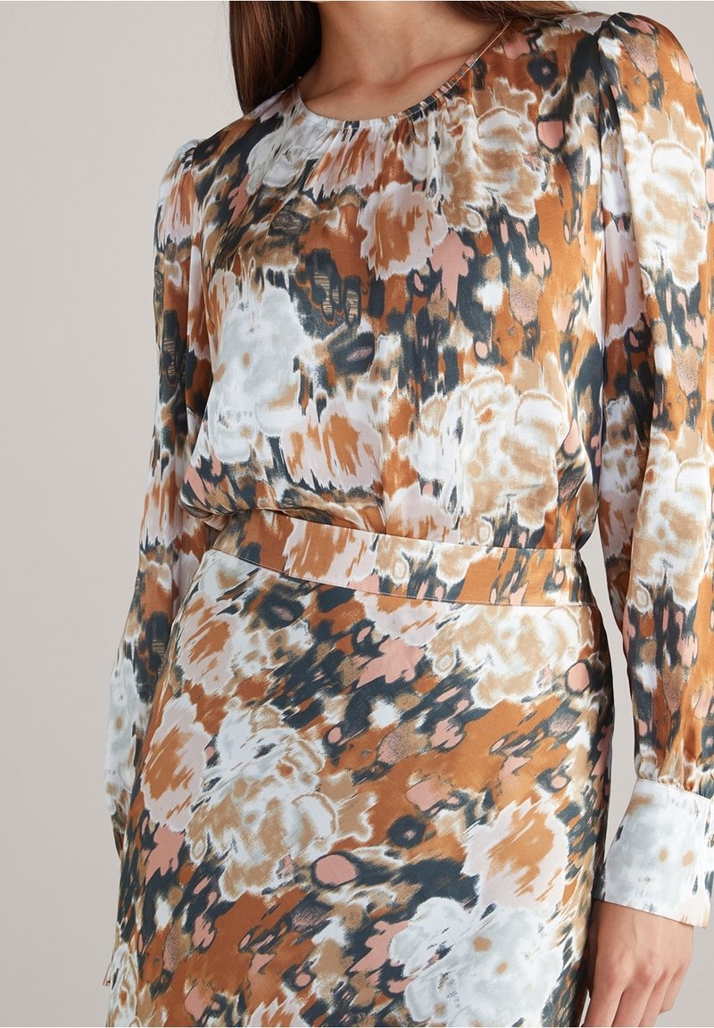 Femme portant une robe à manches longues avec un motif floral abstrait aux tons marron, blanc, noir et pêche.