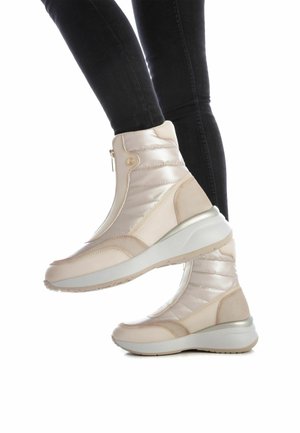 Botas de tobillo beige con forro acolchado, cierre de cremallera, tejido texturizado, suelas en contraste y sutiles acentos metálicos.
