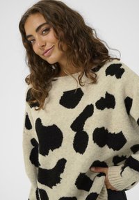 Bēša adīta džemperis ar lieliem melniem govju rakstiem, apaļu dekoltē, nolaistām plecu daļām un ribotiem aprocēm. Mīksta tekstūra un brīva piegriezuma.