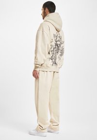 Kremfarget oversized hettegenser med et grafisk design på ryggen. Kombinert med matchende avslappende bukser og hvite sneakers.