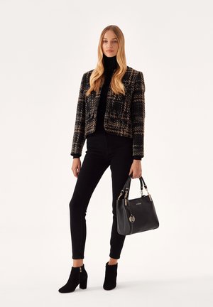 Giacca in tweed nera a maniche corte con accenti arancioni e oro, dolcevita nera, jeans neri aderenti, stivali alla caviglia neri in suede e borsa nera.