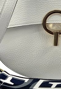 Witte lederen handtas met een gestructureerde afwerking, uitgerust met een ronde gouden sluiting en een marineblauwe stoffen schouderband met abstracte patronen.