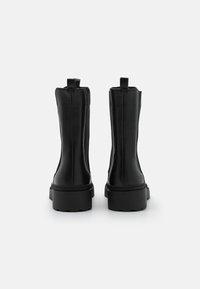 Botines de cuero negro con textura suave, que cuentan con una suela gruesa, tiradores y costuras continuas a lo largo de los lados.