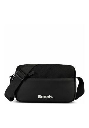 Sac bandoulière noir présentant une partie inférieure en cuir lisse et une partie supérieure en tissu texturé. Bandoulière ajustable et logo "Bench." argenté affiché.