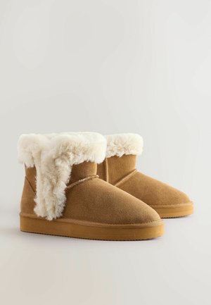 Bruna mockaskinnsankleboots med en fluffig vit fuskpälskrage, rund tå och platt gummisula. Sömnadsdetaljer längs sidorna.