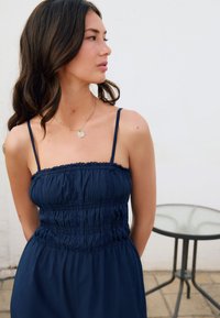 Vestido azul marino sin mangas con detalles fruncidos. Tejido suave, cintura elástica y delicados bordes con volantes. Diseño minimalista.