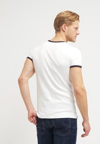 Weißes Baumwoll-T-Shirt mit navyblauer Ripp-Kragen und -Ärmelabschlüssen, taillierte Passform, von hinten gezeigt, kombiniert mit dunkelblauen Jeans.