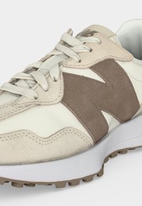 Baskets beige et blanches avec logo « N » en daim taupe, lacets blancs et semelle en caoutchouc marron clair texturée.