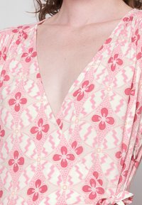 Rosa Kleid mit Blumenmuster und tiefem V-Ausschnitt, aus strukturiertem Stoff, mit gerafften Details und einer gebundenen Verzierung an einer Seite.