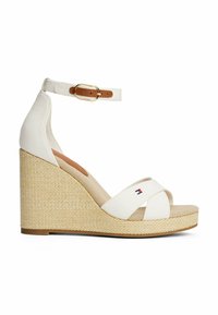 Sandalias de cuña blancas con tiras de lona entrecruzadas, correa de tobillo color tostado con un hebilla dorada y una base de plataforma tejida texturizada. Detalle del logo en rojo y azul.
