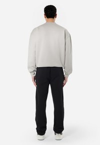 Lys grå sweatshirt med afslappet pasform og sænkede skuldre, parret med sorte bukser. Sweatshirten har en blød tekstur og ribbede manchetter.