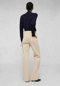 Top de manga larga azul marino combinado con pantalones de pierna ancha beige, con una cintura alta y dos bolsillos traseros. Tacones negros de punta completan el atuendo.