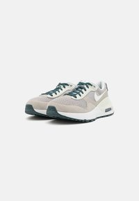 Sneakers Nike con una tomaia in mesh beige e grigio chiaro, lacci verde scuro, dettagli in suede e una suola intermedia bianca, dotate di un'unità air visibile.