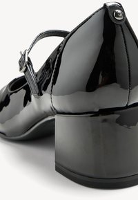 Black patent leather Mary Jane shoes with a rounded toe, ankle strap, and a block heel. Smooth, shiny surface with minimal hardware detailing.