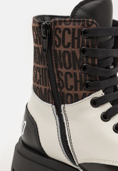 Bottes montantes avec un orteil en cuir blanc, des accents en cuir noir, un tissu à motifs marron, un laçage à l'avant et une fermeture éclair sur le côté pour un enfilage facile.