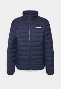 Mörkblå pufferjacka med dragkedja, hög krage, horisontell sömnad och en svart logotyp på vänster bröst.