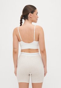 Balta vertikali dryžuota bralette su reguliuojamomis petnešėlėmis, derinama su šviesiai smėlio spalvos aukštu liemeniu šortais, turinčiais kontrastingą baltą juosmens detalę.