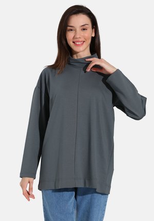 Gray, long-sleeve top with a high neckline, featuring a relaxed fit, soft texture, and seam detailing, paired with blue jeans.