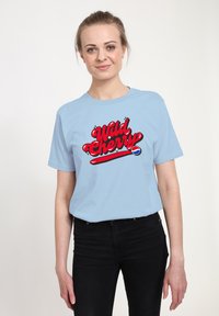Světle modré bavlněné tričko s velkou červenou grafikou "Wild Cherry" s lesklým povrchem a detailním logem na spodu.