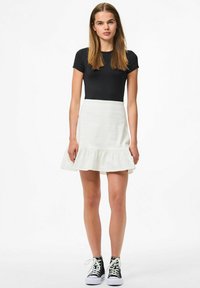 Melnas īsām piedurknēm blūze kombinēta ar balto volānu svārku, kuram ir gluda tekstūra un ikdienišķs stils, papildināts ar melniem augstiem sporta apaviem.