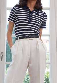 Marineblauwe en witte gestreepte poloshirt met een knoopsluiting, gecombineerd met hooggesneden lichtbeige broeken en een zwarte riem met een zilveren gesp.