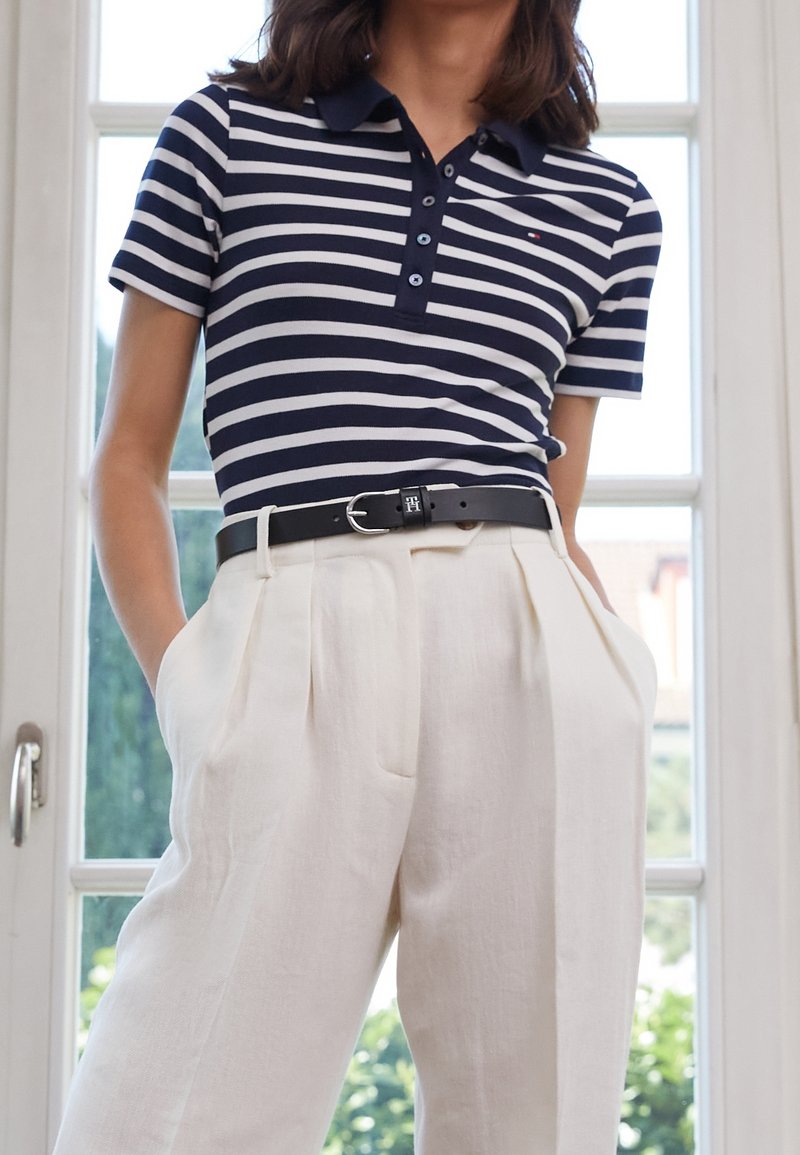 Marineblauwe en witte gestreepte poloshirt met een knoopsluiting, gecombineerd met hooggesneden lichtbeige broeken en een zwarte riem met een zilveren gesp.