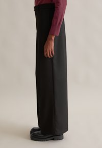 Zwarte wijde broek gemaakt van gladde stof, met een hoge taille en subtiele zijnaaddetails, gecombineerd met chunky zwarte schoenen.