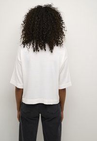 White short-sleeve top with a relaxed fit, featuring a rounded hem and ribbed neckline, paired with high-waisted black denim jeans.