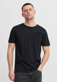 Camiseta de algodón negra con mangas cortas, cuello redondo y un bolsillo parchado en el lado izquierdo del pecho. Tejido texturizado y corte relajado.
