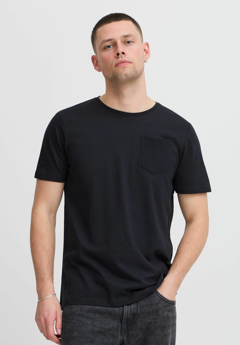Camiseta de algodón negra con mangas cortas, cuello redondo y un bolsillo parchado en el lado izquierdo del pecho. Tejido texturizado y corte relajado.