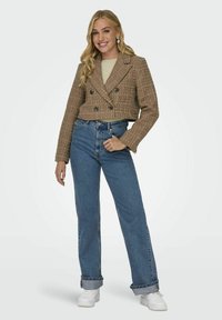 Veste cropped texturée marron avec boutons double boutonnage, associée à un jean en denim bleu taille haute et des baskets blanches.