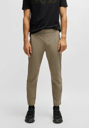 Lettere, tapered bukser i beige med elastisk talje og sidelommer. Stof med en glat tekstur. Båret med en sort T-shirt og sorte sneakers.