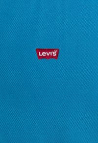 Tejido texturizado de un brillante color azul con un pequeño parche del logo de Levi's en rojo bordado en hilo blanco en el centro.