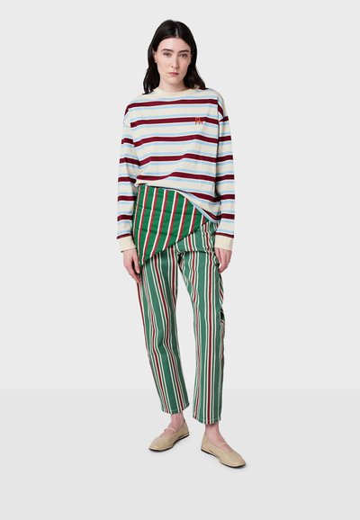 Pasiasta koszula z długim rękawem w kolorze kremowym, niebieskim i burgundowym. Zielono-czerwone spodnie w paski z unikalnym, drapowanym pasem. Beżowe mokasyny.