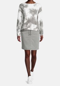 Sudadera gris con diseño tie-dye, con cuello redondo y mangas largas, combinada con una falda de mezclilla gris hasta la rodilla y zapatillas blancas.