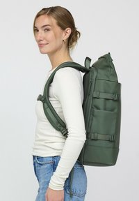 Grüner wasserdichter Rucksack mit verstellbaren Trägern, einem oberen Griff und externen Taschen. Schlanker, rechteckiger Form mit einer glatten Textur.