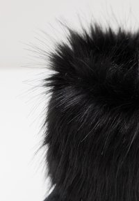 Czarna sztuczna futro z długimi, miękkimi włóknami, tworzącymi puszystą teksturę. Projekt charakteryzuje się zaokrąglonym kształtem, akcentującym miękki materiał.
