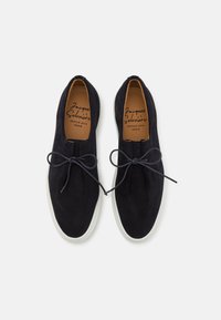 Schwarze Wildlederschuhe mit runder Zehenform, kontrastierender weißer Gummisohle und gebundenen schwarzen Schnürsenkeln, ausgestattet mit einem glatten Innenfutter.