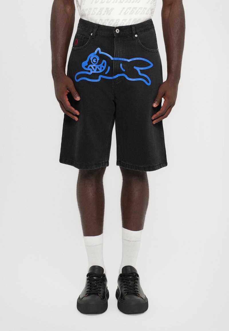 Shorts de mezclilla negra con un gran gráfico azul de un gato, bolsillos laterales y un ajuste relajado; combinados con zapatos negros y calcetines blancos.