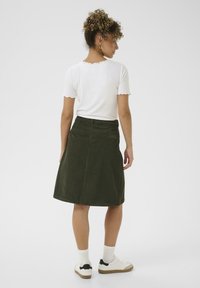 Khaki groene corduroy rok met een op maat gemaakte taille en subtiele plooien, gecombineerd met een witte geribde T-shirt en casual witte sneakers.
