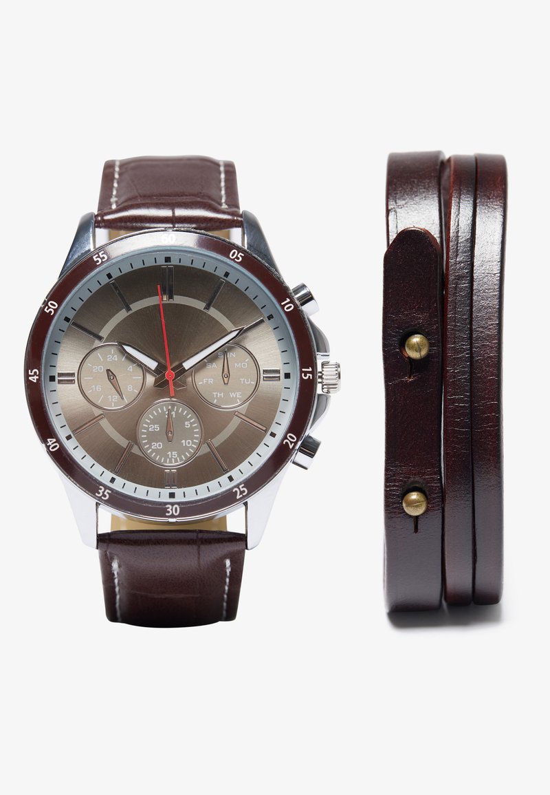 Reloj con correa de cuero marrón, caja metálica plateada, esfera gris, segundero rojo y subesferas. Presenta un acabado pulido y acentos en contraste.