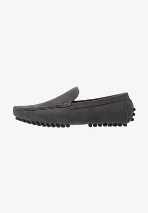 Mocassin homme en daim gris avec des picots en caoutchouc sur la semelle et le talon, style slip-on, coutures détaillées le long des bords, vue latérale sur fond blanc.