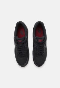 Černé tenisky Nike s pletivovým svrškem, texturovanými detaily, červenými stélkami a šněrováním. Kulatá špička a kontrastní bílá podrážka.